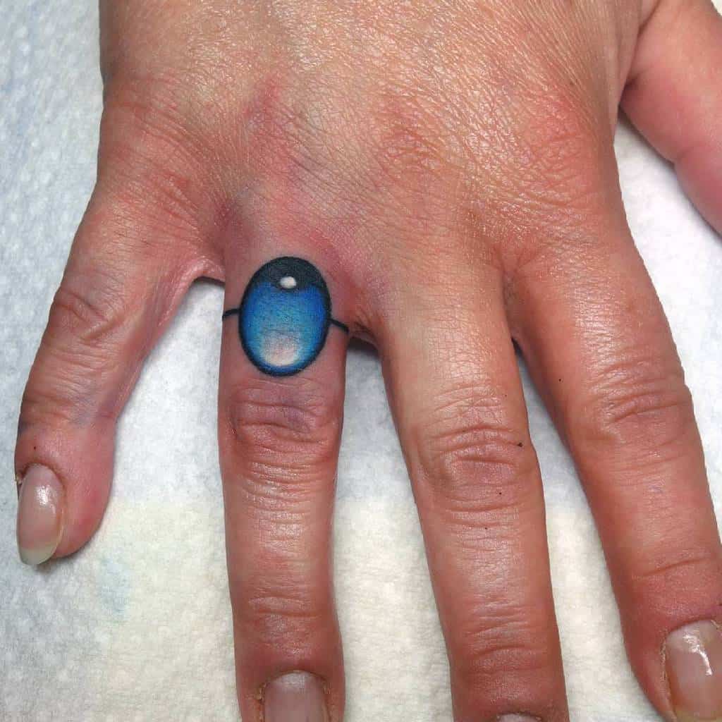 Hand with a ring tattoo on the finger, resembling a blue stone