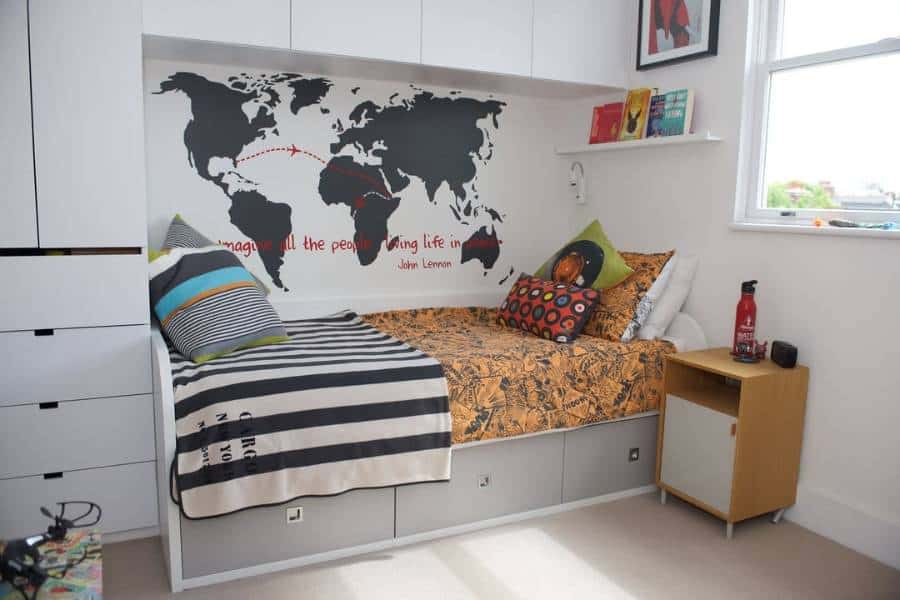 Single bed with storage drawers, world map wallpaper, and colorful pillows.