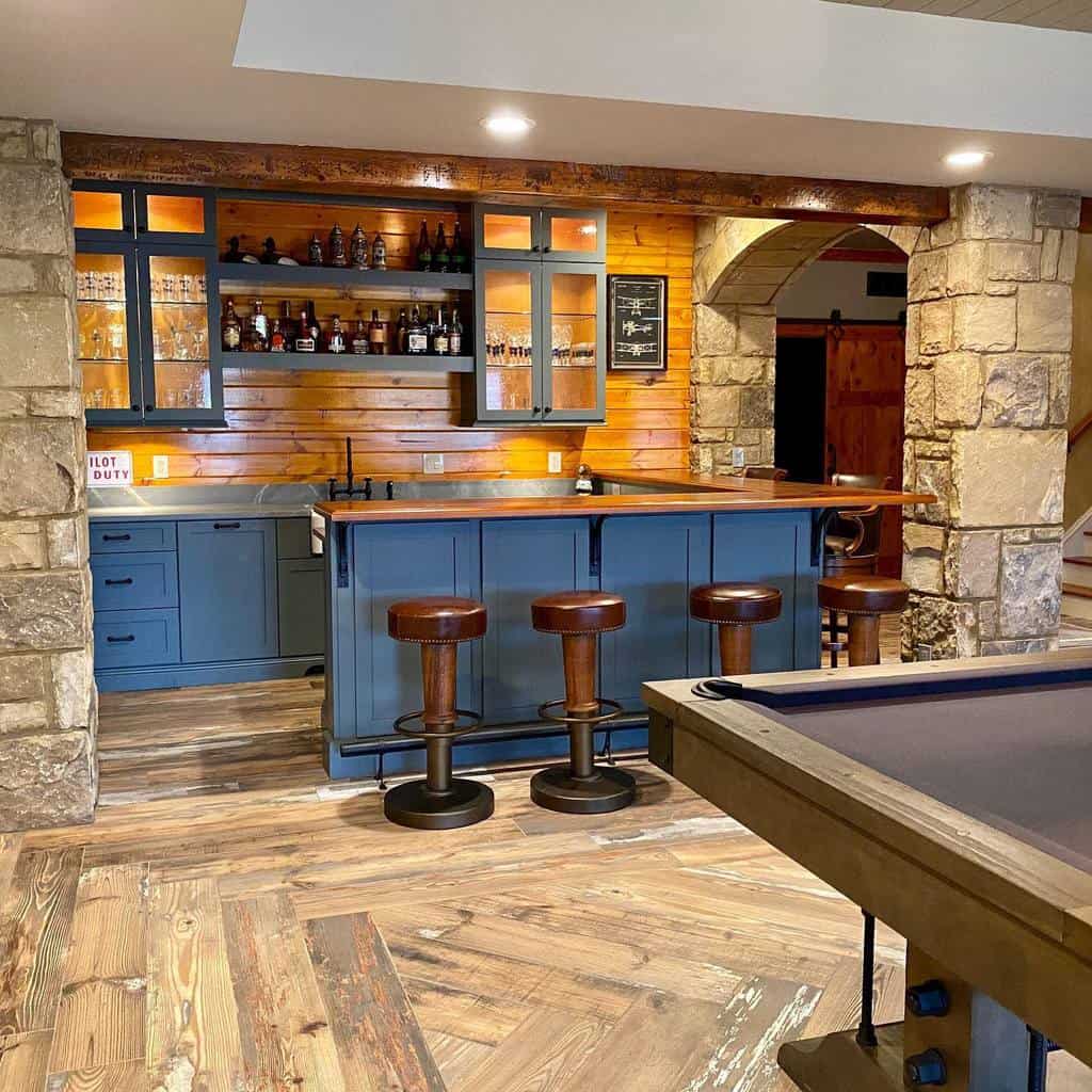 Rustic corner basement bar with stone columns, wood accents, and blue cabinetry featuring leather stools.