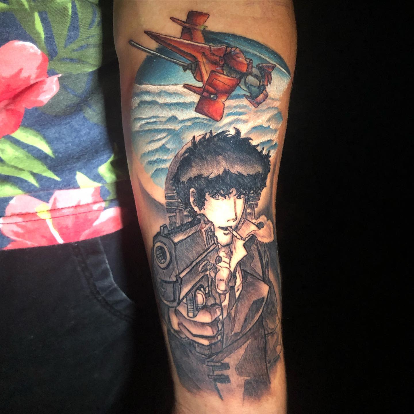 Forearm tattoo of Spike Spiegel from Cowboy Bebop, holding a gun with the Swordfish II flying above, set against a cloudy sky background