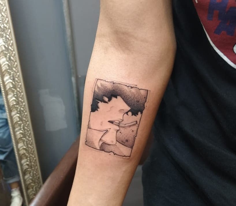 Small forearm tattoo of Spike Spiegel from Cowboy Bebop, smoking a cigarette with a shaded effect, framed within a weathered rectangular outline