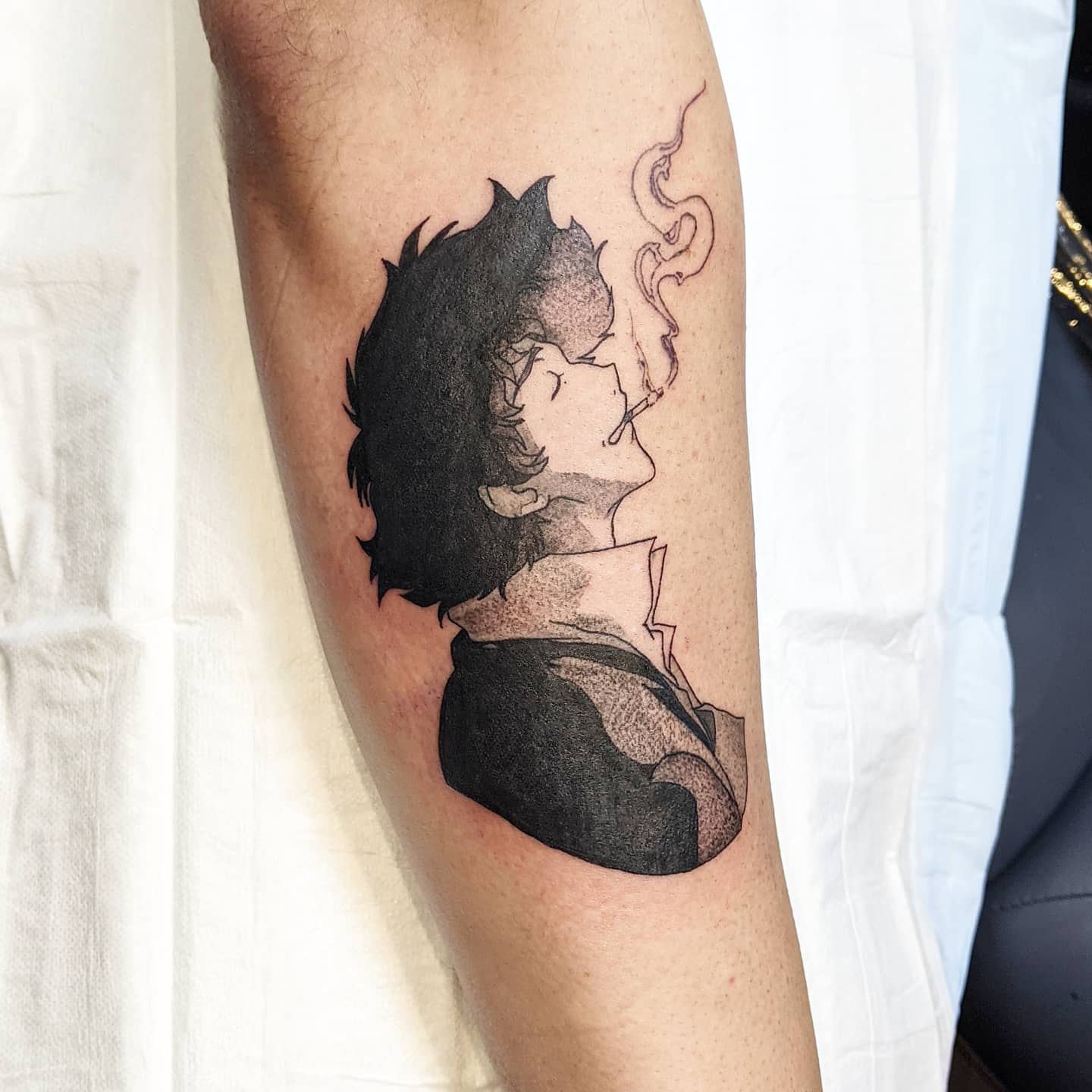 Tattoo of Spike Spiegel from Cowboy Bebop, exhaling smoke with a calm expression, shaded in black and gray