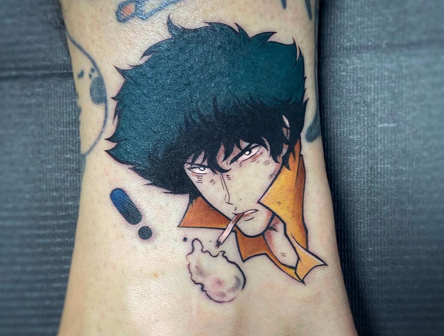 Small tattoo of Spike Spiegel from Cowboy Bebop, with a focused expression, smoking a cigarette, and highlighted with bold colors