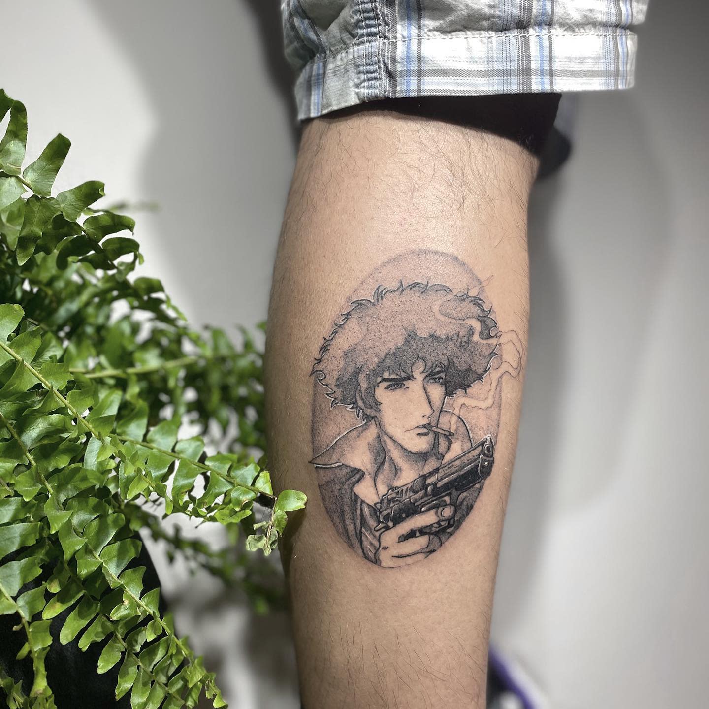 Small tattoo of Spike Spiegel from Cowboy Bebop, holding a gun and smoking a cigarette, within an oval frame