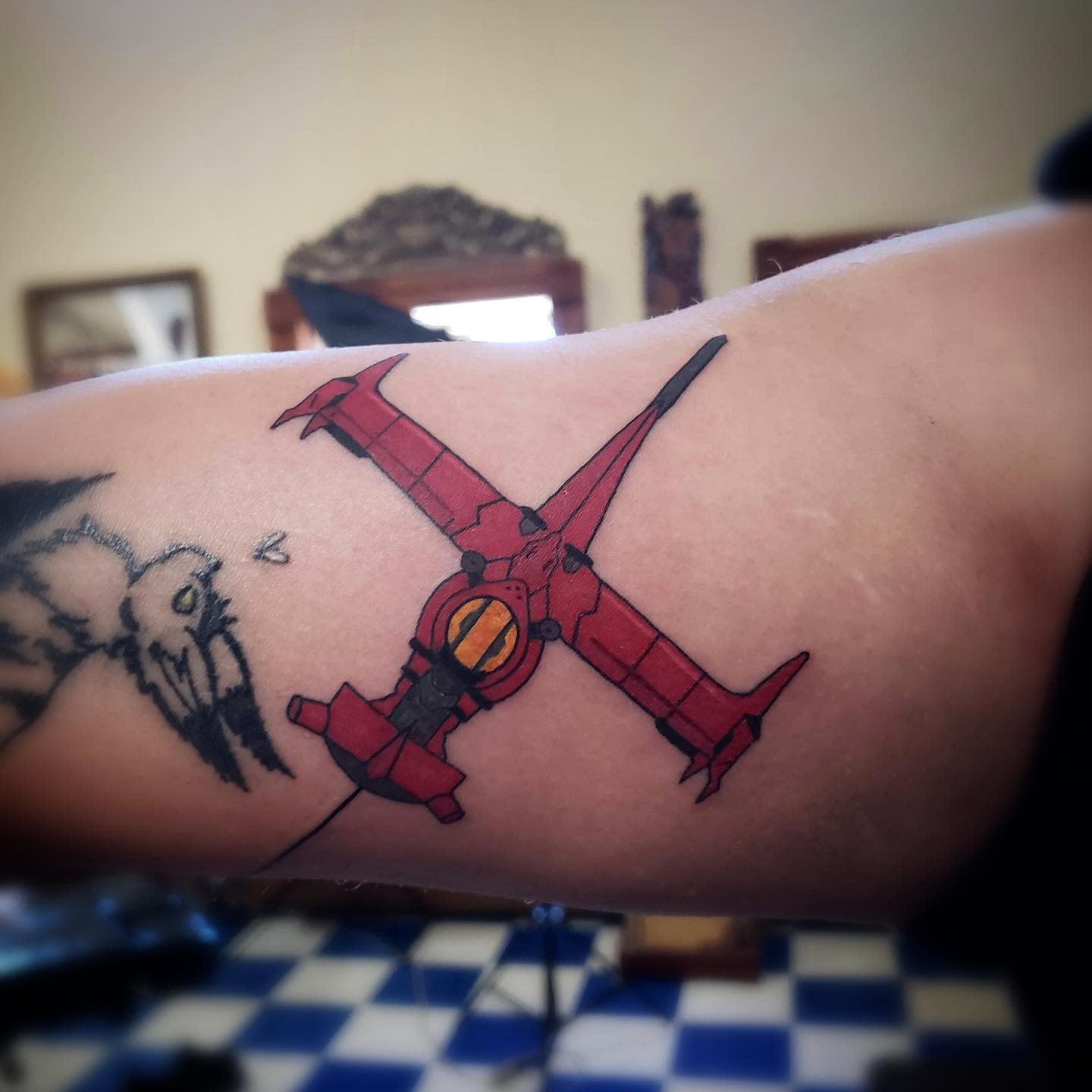 Tattoo of the Swordfish II spaceship from Cowboy Bebop, inked in red with a simple and bold design on the bicep
