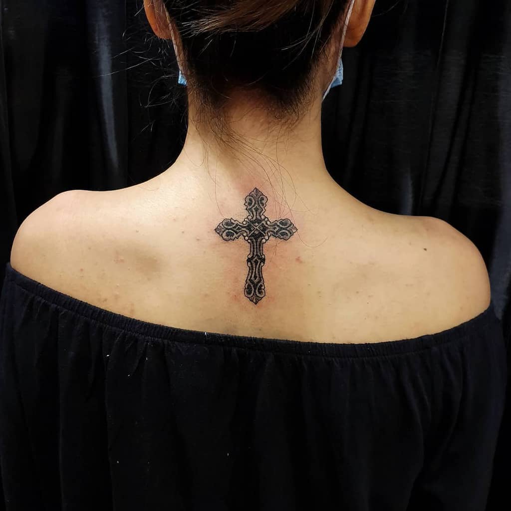 Ornate cross tattoo on woman's upper back and neck