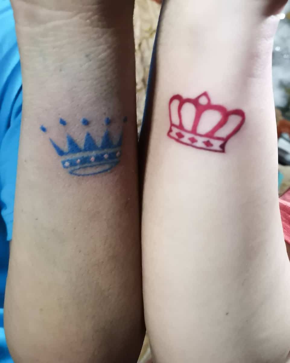 Two forearms with matching crown tattoos; left tattoo is blue, right tattoo is red