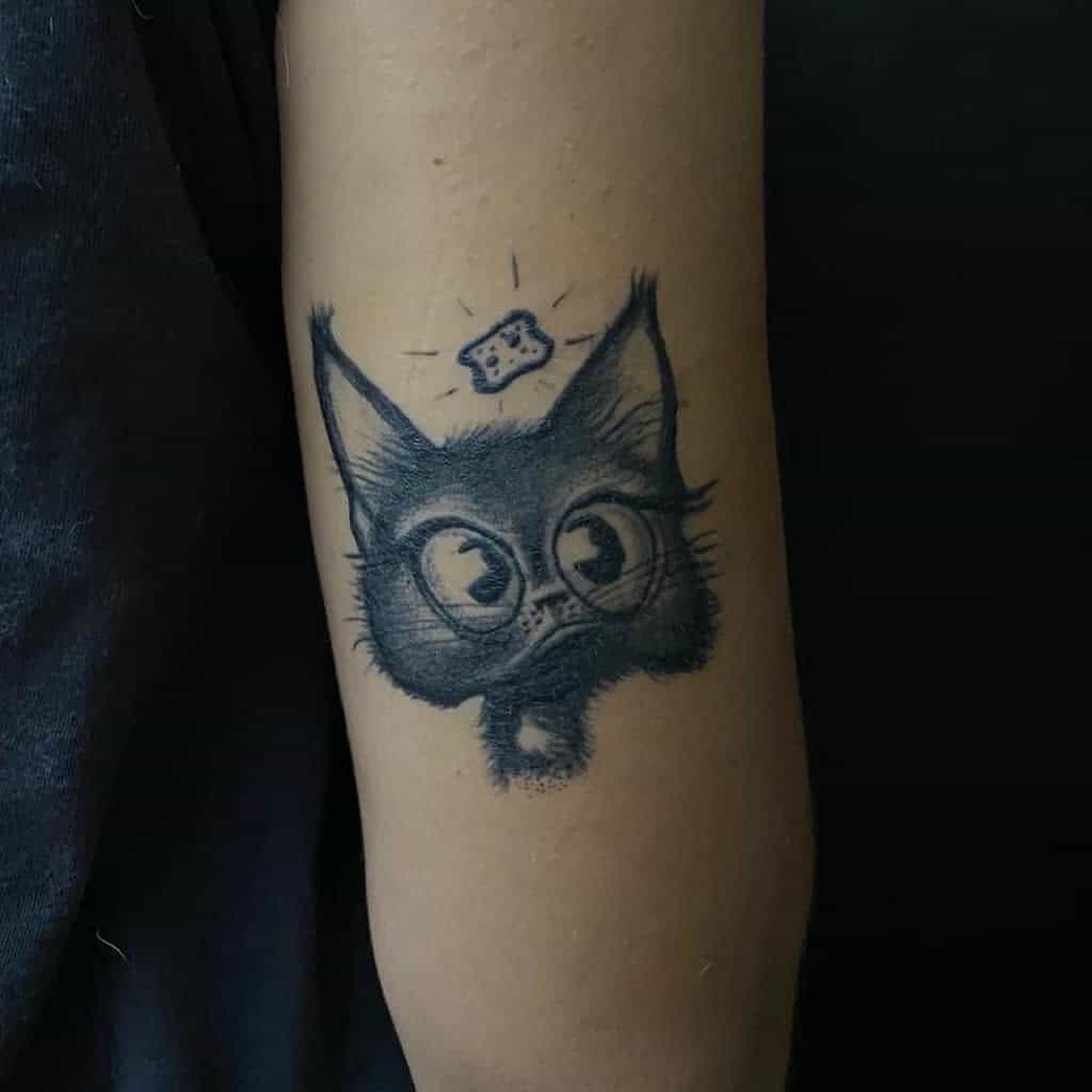 Tattoo of a whimsical cartoon cat on an arm, looking up at a small, floating cracker
