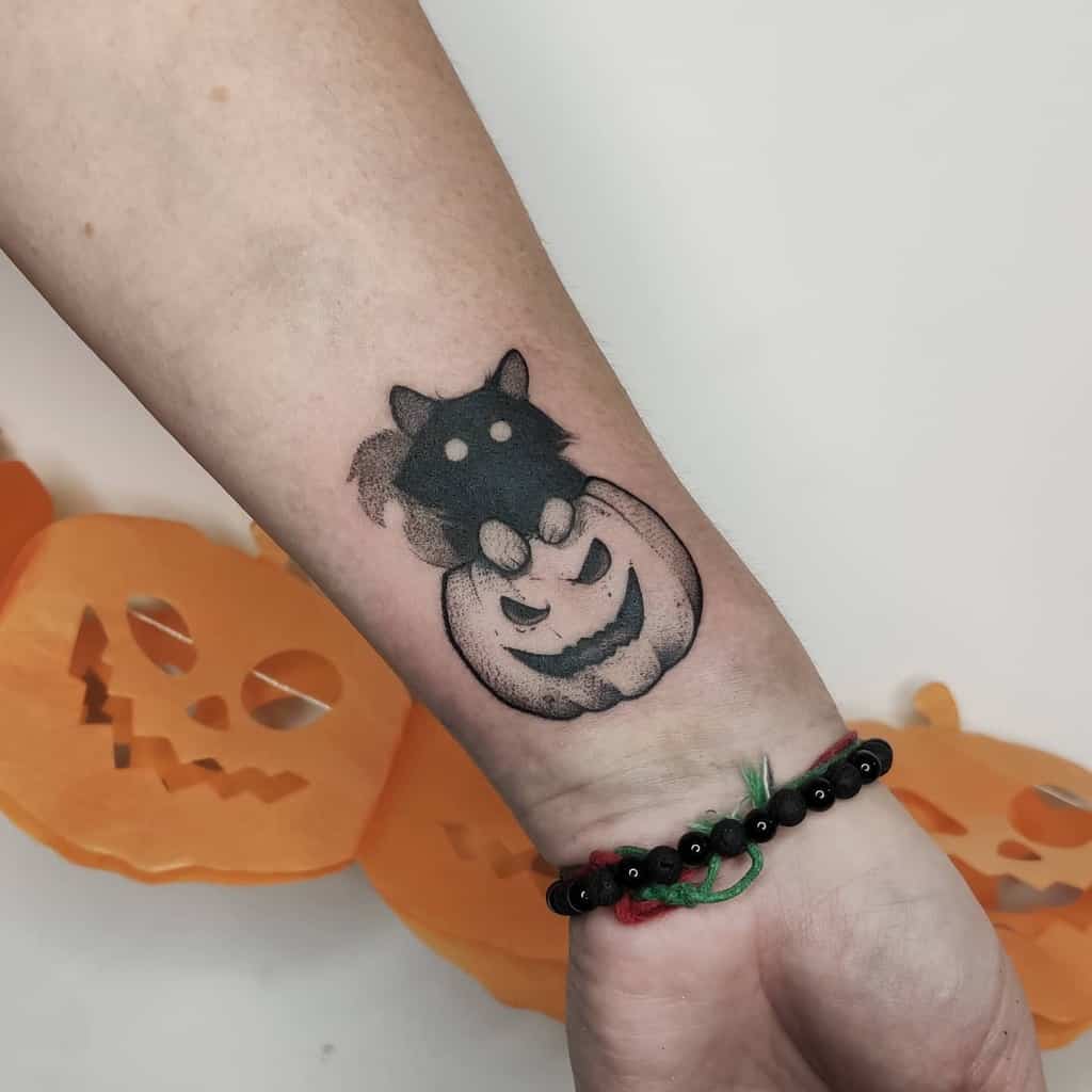 Tattoo of a black cat peeking over a jack-o'-lantern on a person's forearm, the cat's curious eyes adding a touch of mystery