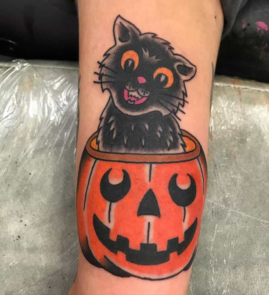 Tattoo of a mischievous black cat popping out of a smiling jack-o'-lantern on a person's arm