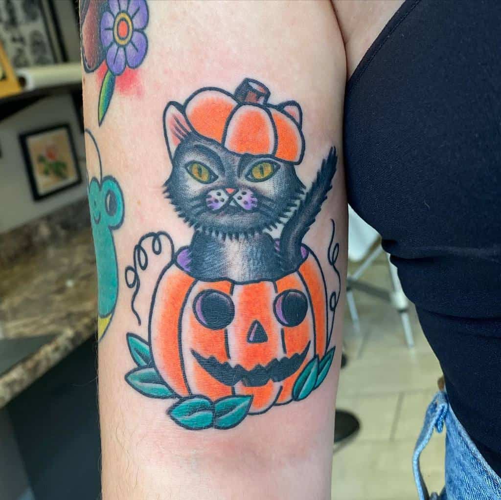 Tattoo of a cat nestled in a black pumpkin on upper arm