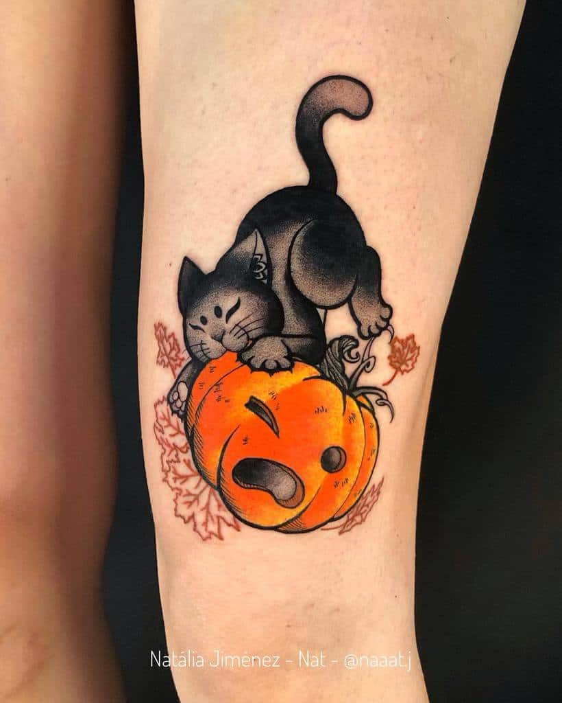 A black cat is playfully engaged with a carved pumpkin in this intricate tattoo on someone's arm