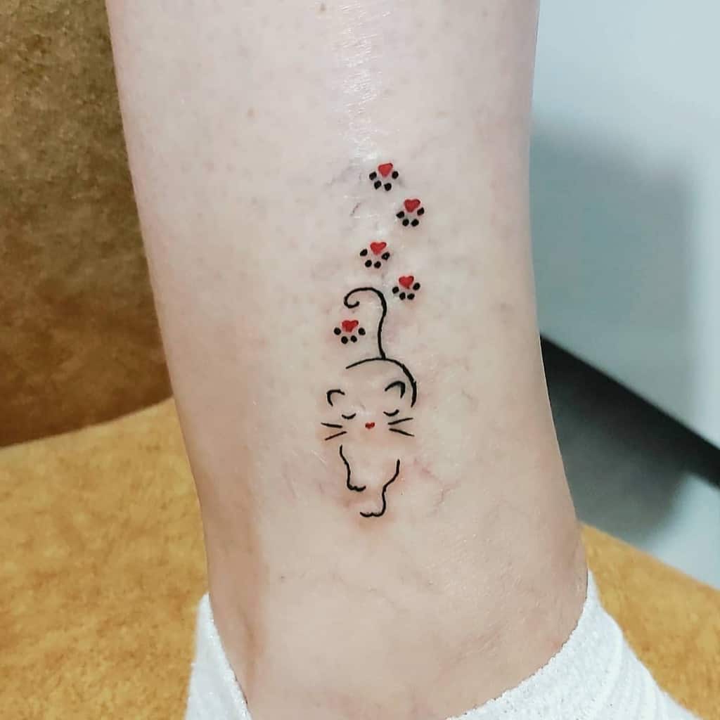 Tattoo of a minimalist cat with delicate paw prints on a person's leg