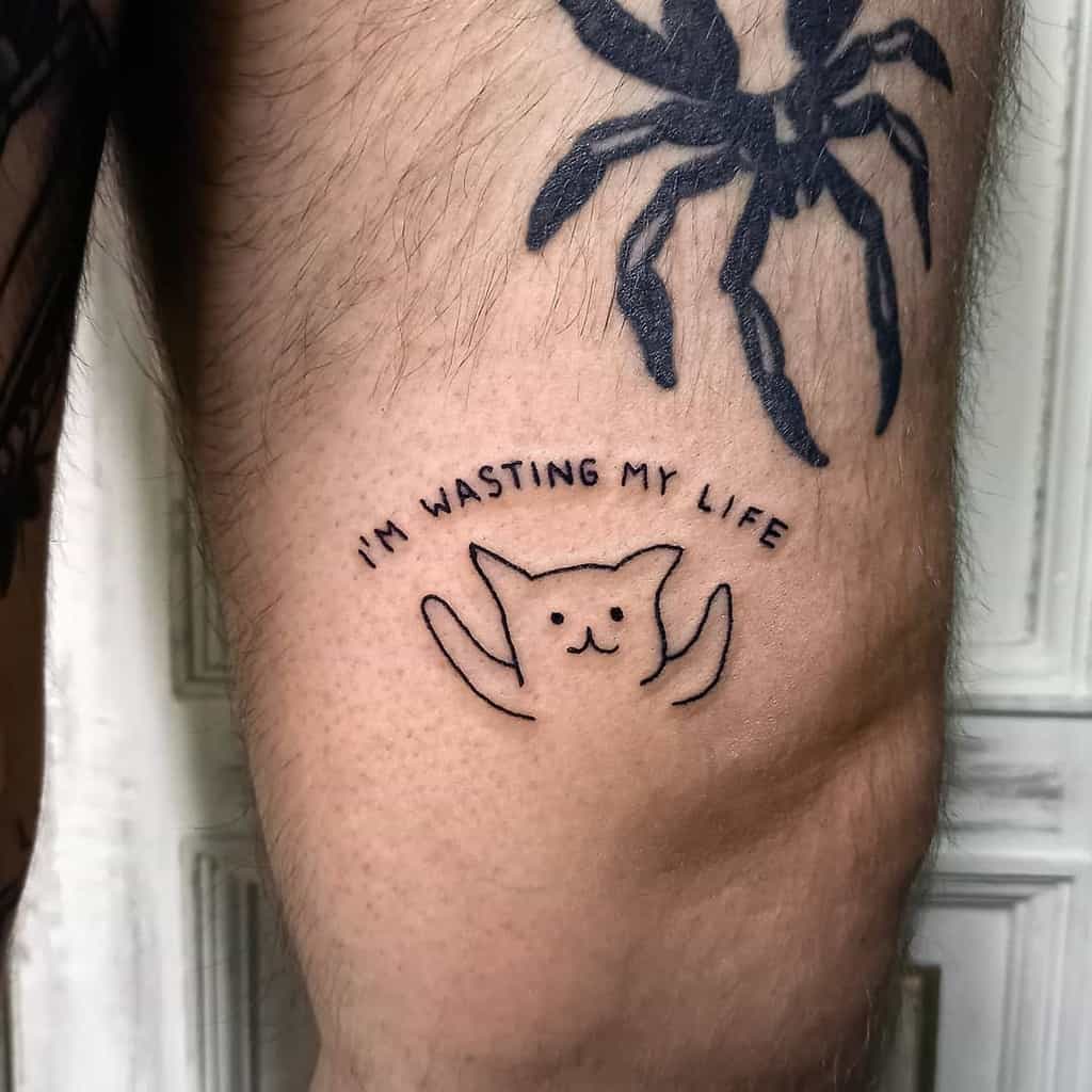 Simple tattoo featuring a cat with the text "I'M WASTING MY LIFE" arched above it