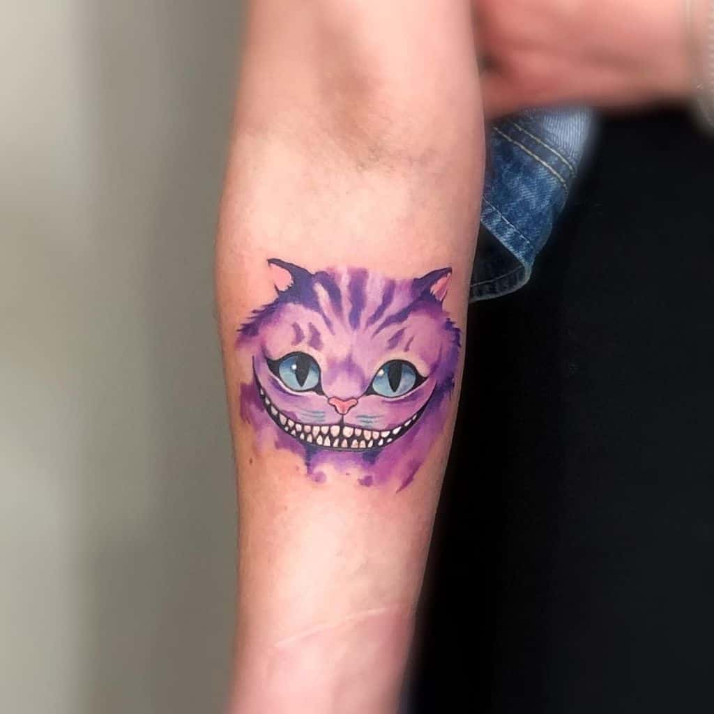 A simple and cute Cheshire Cat tattoo in purple tones, featuring its iconic grin and bright blue eyes