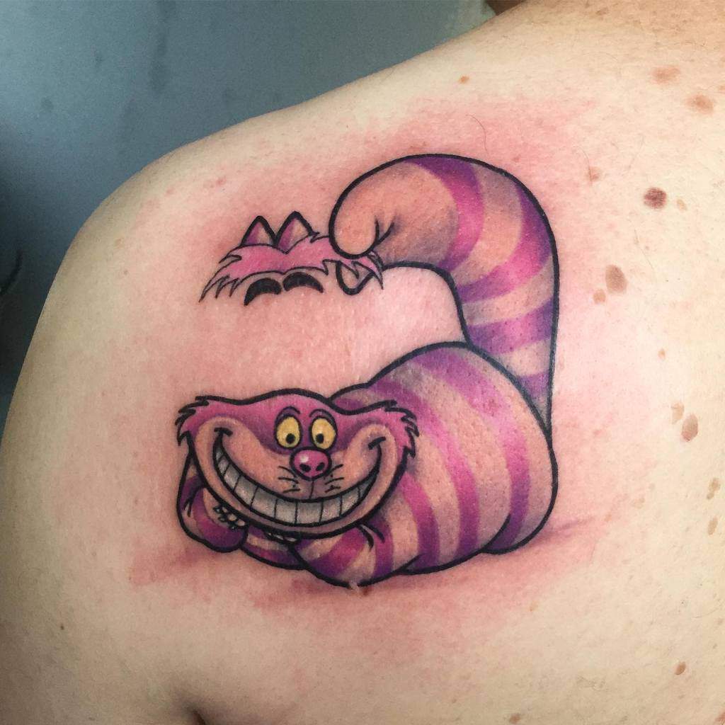 A playful tattoo of the classic Cheshire Cat with a wide grin, in pink and purple stripes, fading away at the top