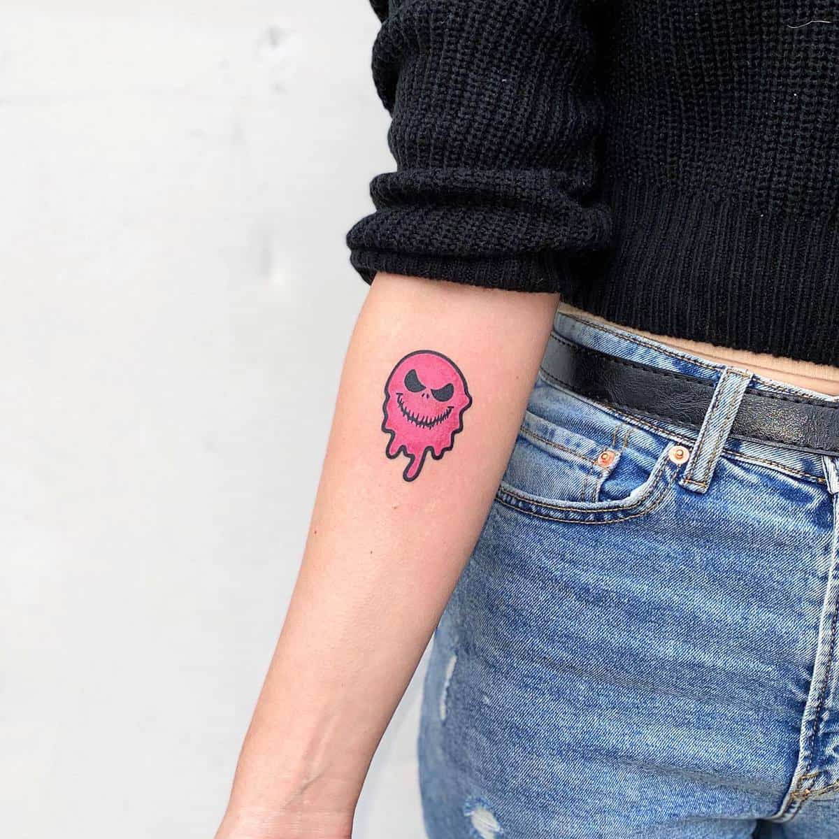 Forearm tattoo of a pink melting smiley face with black eyes and mouth