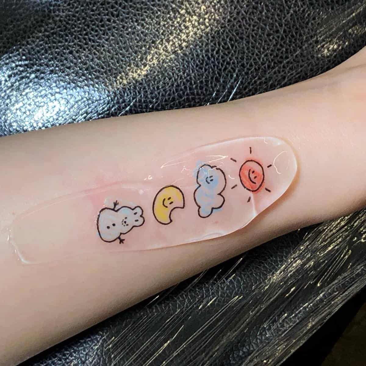 An arm with cute cartoon tattoos of weather symbols: cloud, moon, sun, and star