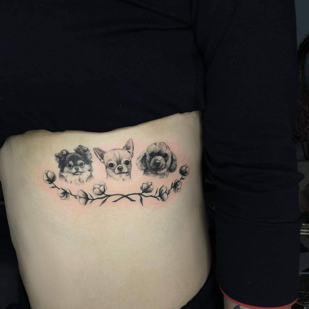 Tattoo of three dog faces with a floral design on ribcage
