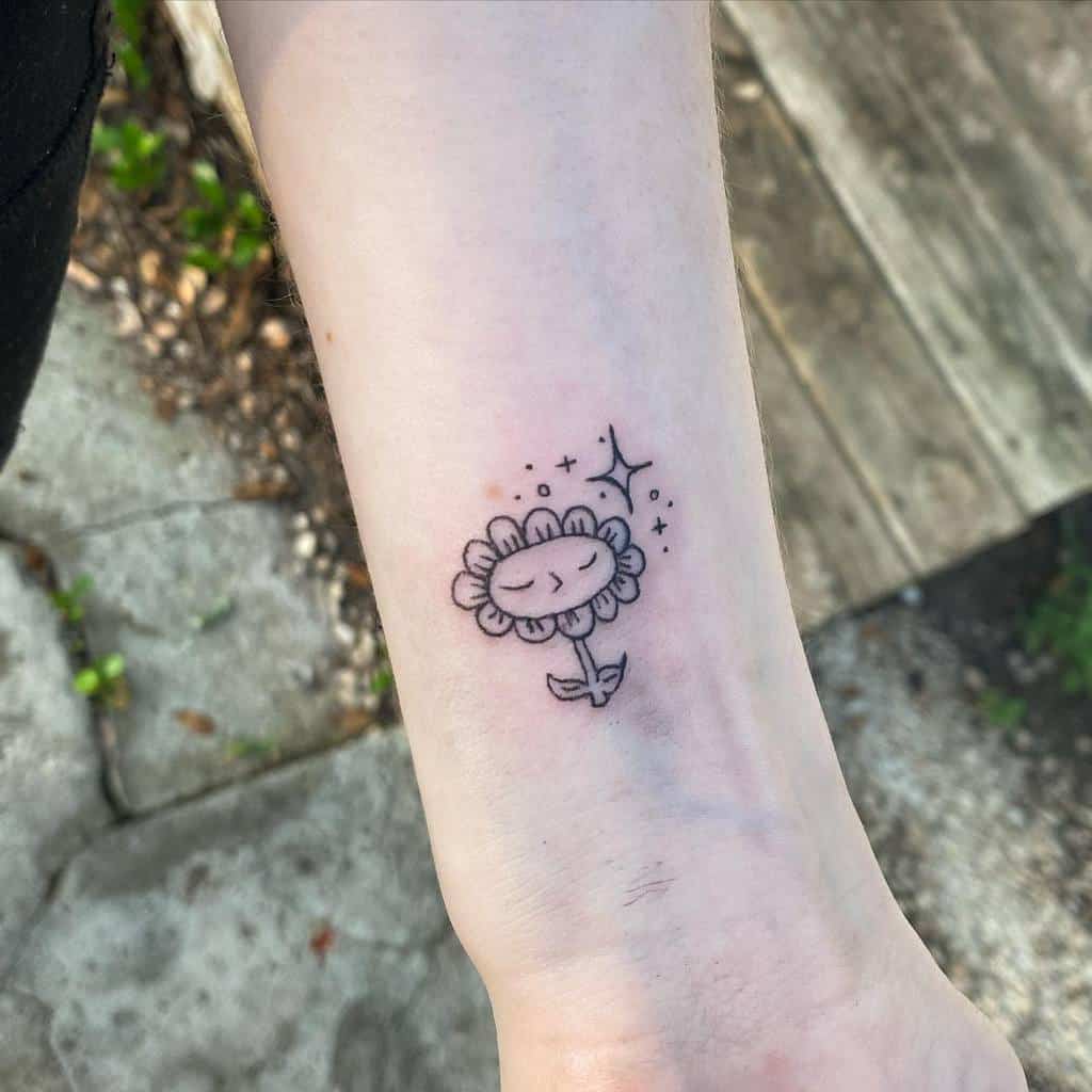 Line art tattoo of a smiling flower with sparkles on a wrist