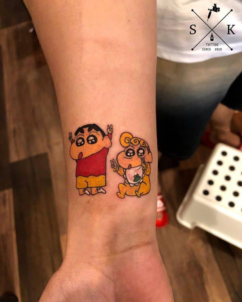 Tattoo of two cartoon characters, one in red and yellow, the other in pink, on a wrist