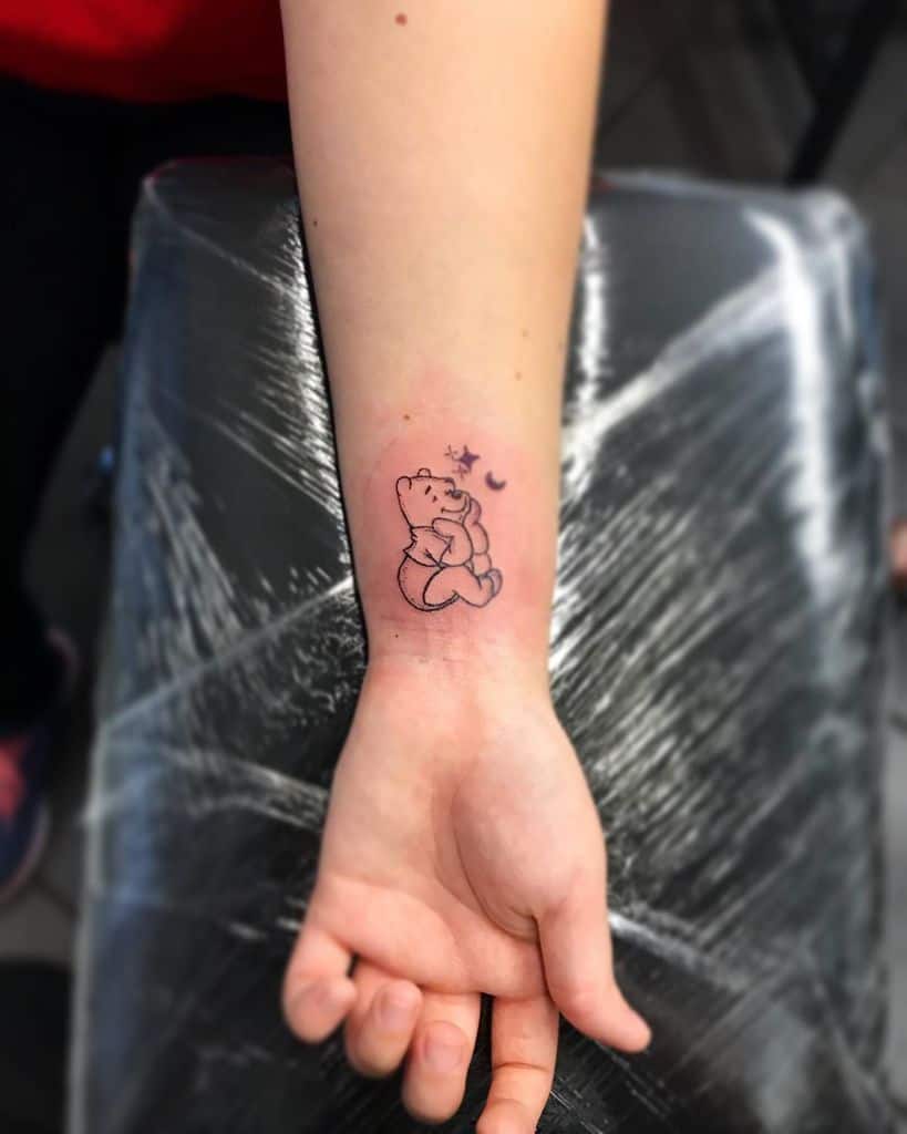 Tattoo of Winnie-the-Pooh on a wrist, with small stars above