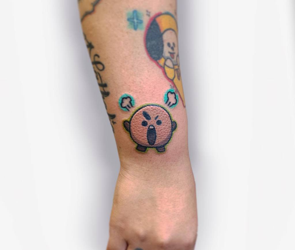 Tattoo of a cartoon-like character, resembling an angry, round creature with open mouth, on a wrist