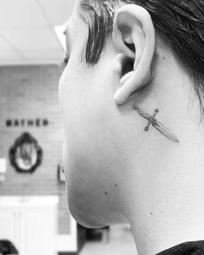 A single needle dagger tattoo behind a person's ear