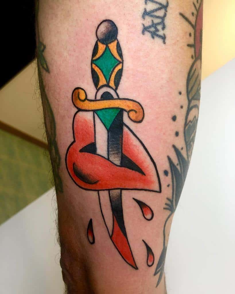 Tattoo of a dagger piercing lips with red droplets and a colorful handle on a person's arm
