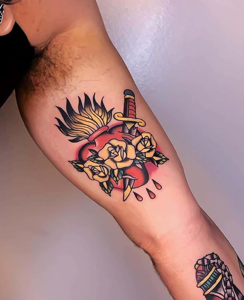 Traditional Sacred Heart tattoo with flames, a dagger, yellow roses, and dripping blood, combining bold colors and classic symbolism