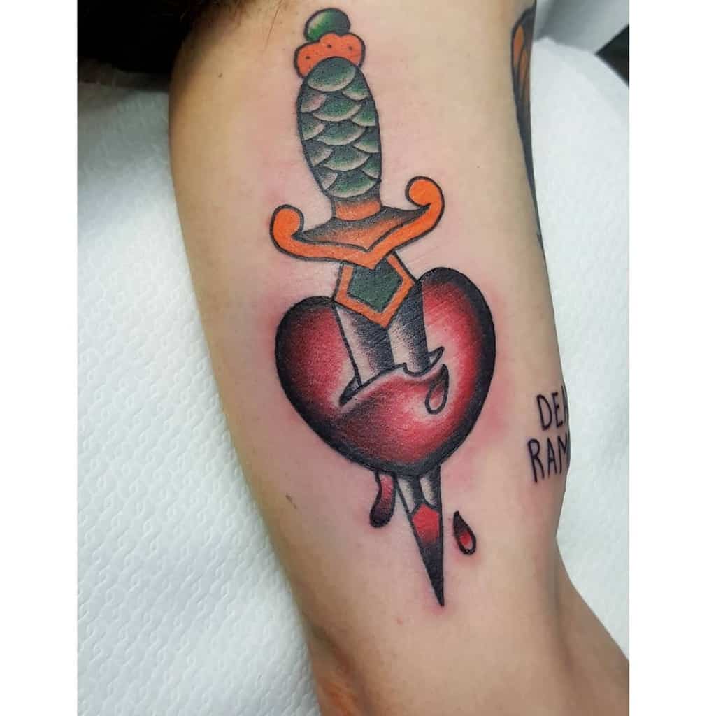 Tattoo of a dagger piercing a heart with bleeding drops on a person's arm