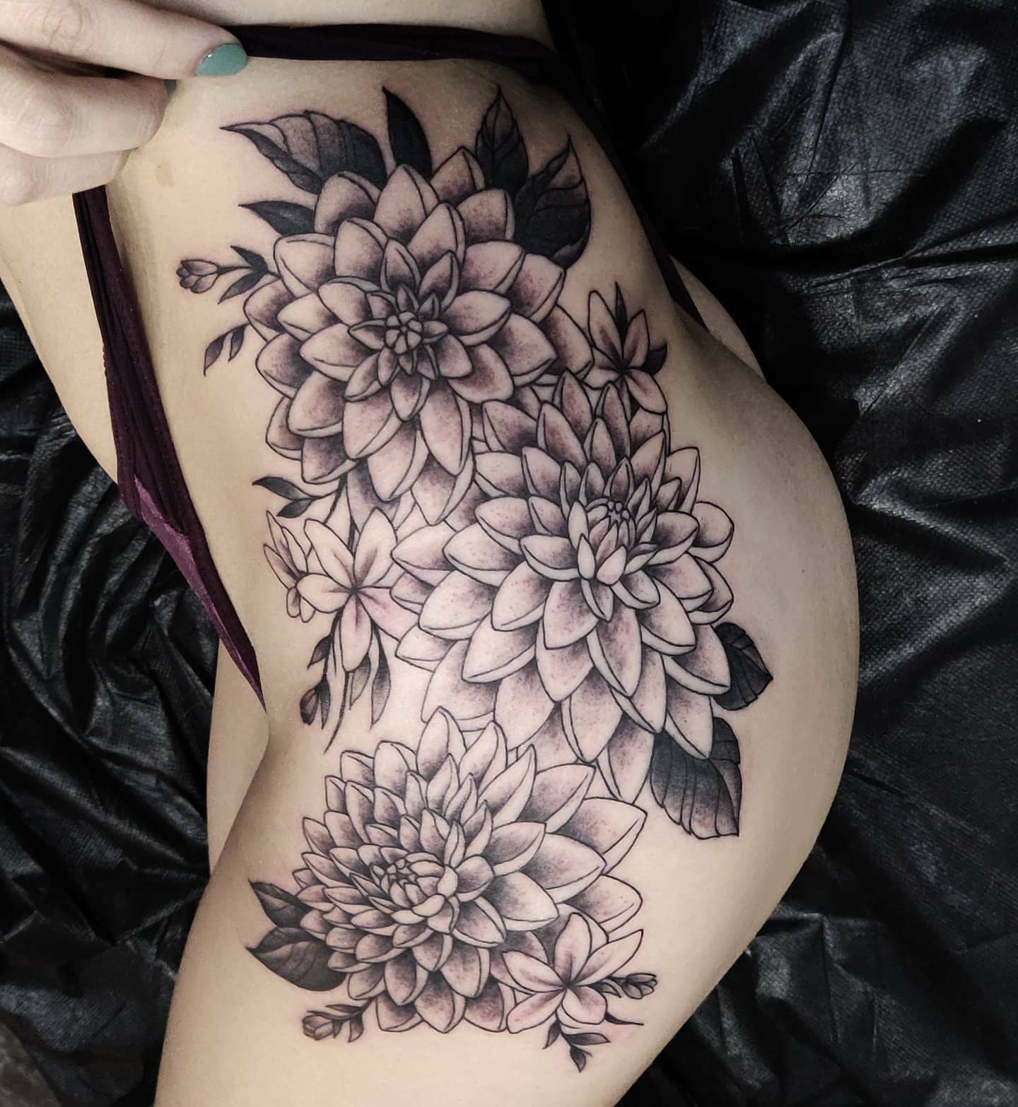 Black and grey flower tattoo on a side, featuring large dahlias and leaves