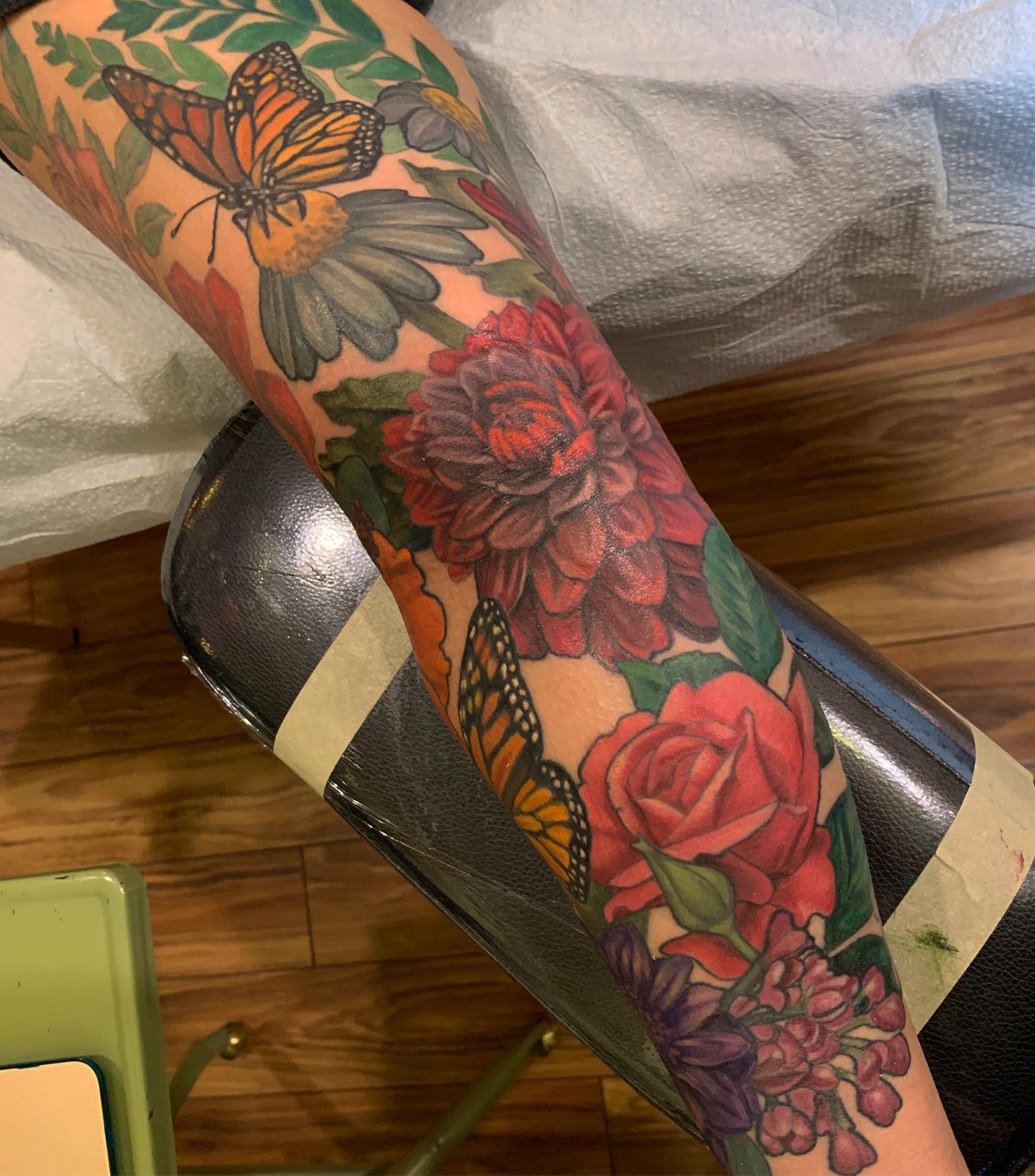 Colorful arm tattoo with dahlia, rose, lilac, daisy flowers, and monarch butterflies