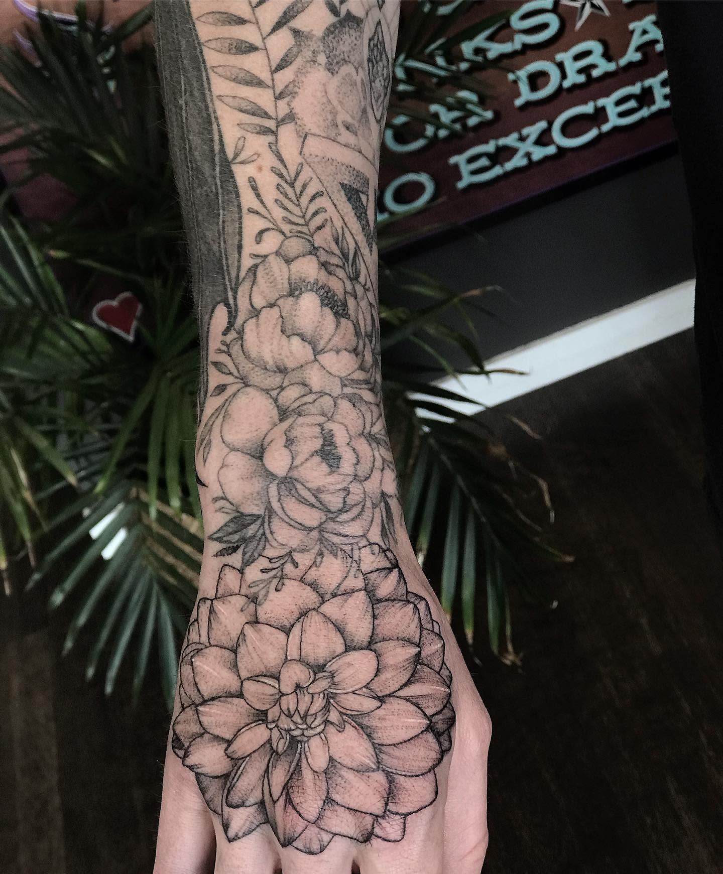 Black and grey tattoo from forearm to hand featuring dahlias and peonies with detailed shading