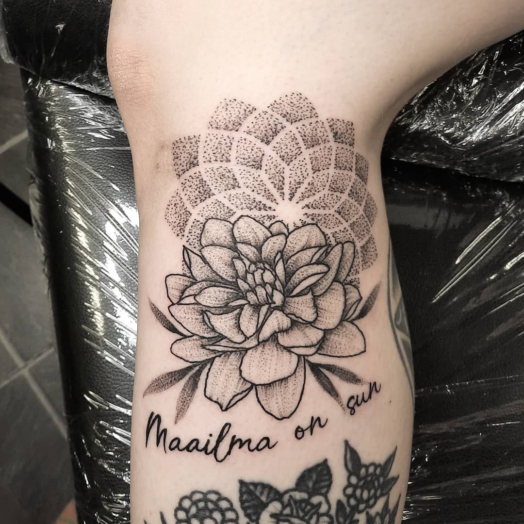 Delicate black and grey dahlia tattoo with geometric pattern and cursive text "Maailma on sun"