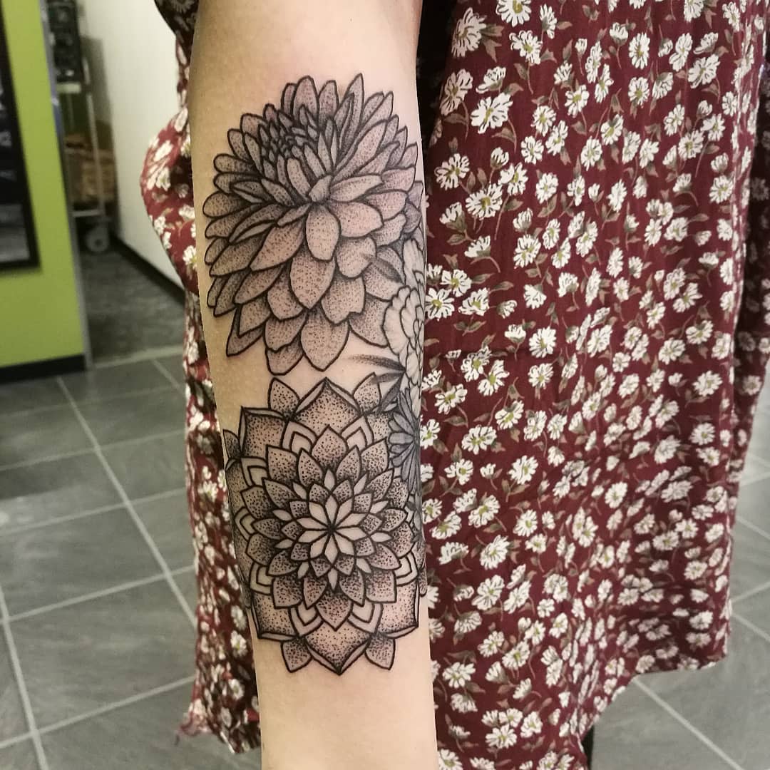 Black and grey forearm tattoo with two detailed dahlia flowers in dotwork style