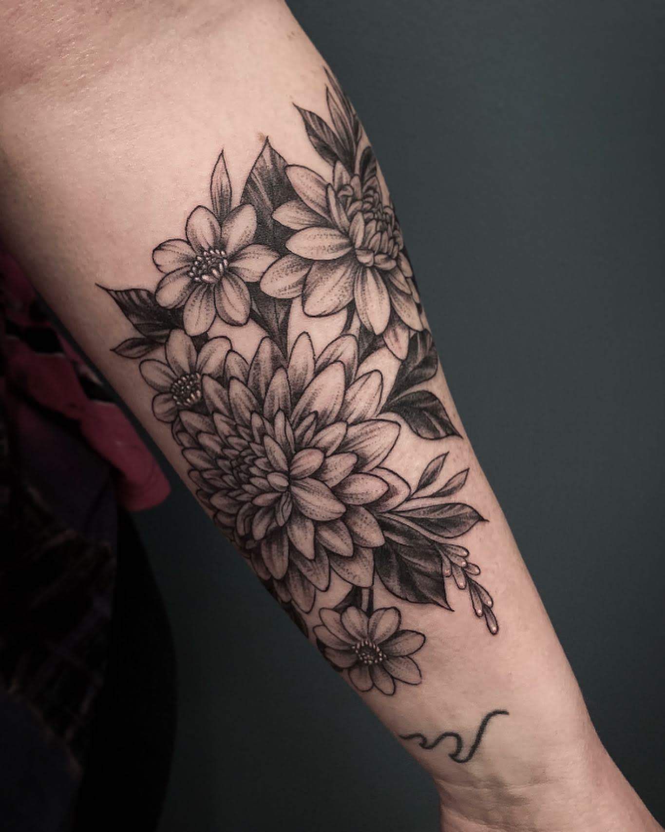 Black and grey forearm tattoo featuring detailed dahlias and smaller daisy-like flowers