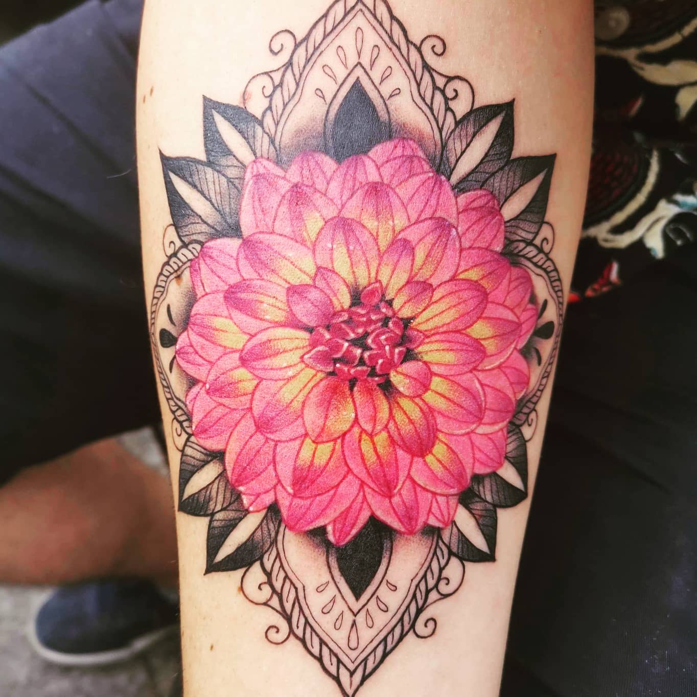Vibrant pink and yellow dahlia tattoo with a decorative mandala pattern surrounding the flower