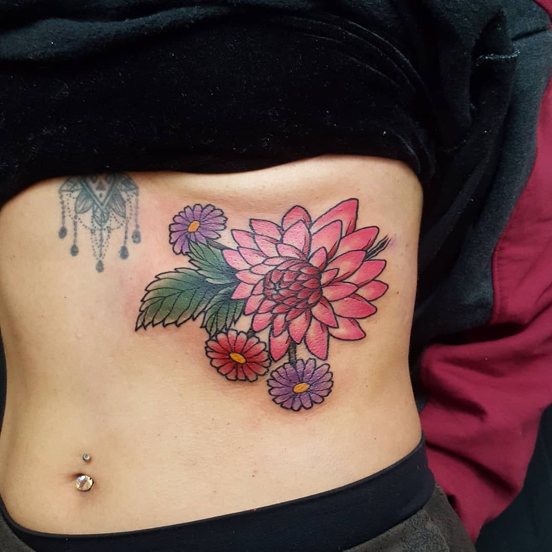 Colorful side torso tattoo with a pink dahlia, purple daisies, and green leave