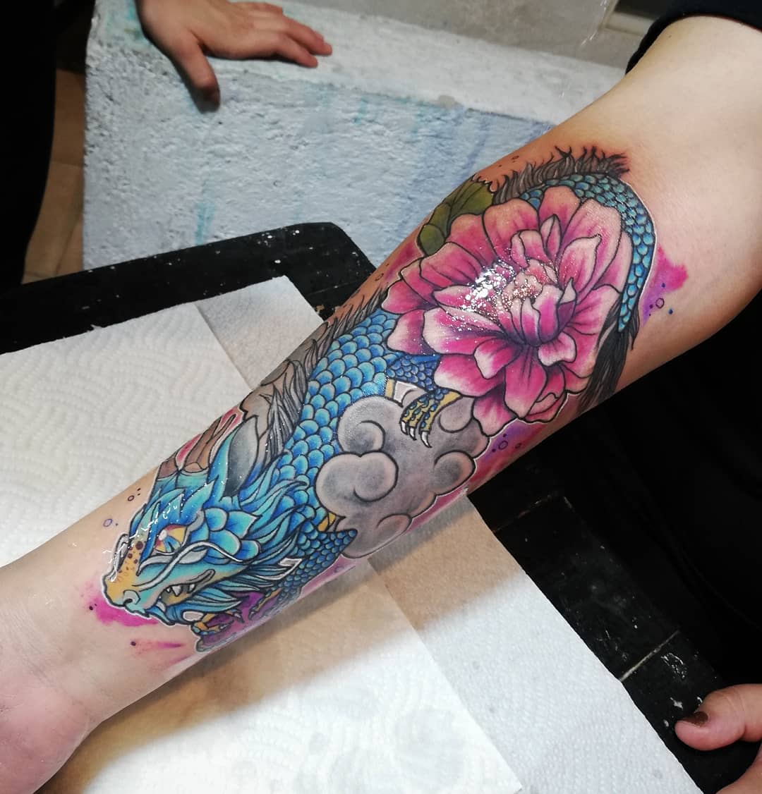 Vibrant forearm tattoo featuring a blue dragon intertwined with a large pink dahlia flower