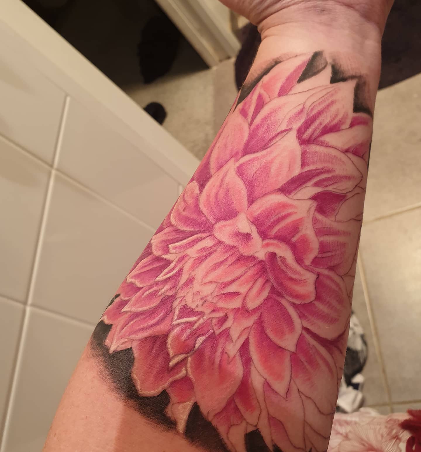 Large pink dahlia tattoo on the forearm with soft gradient shading and detailed petals