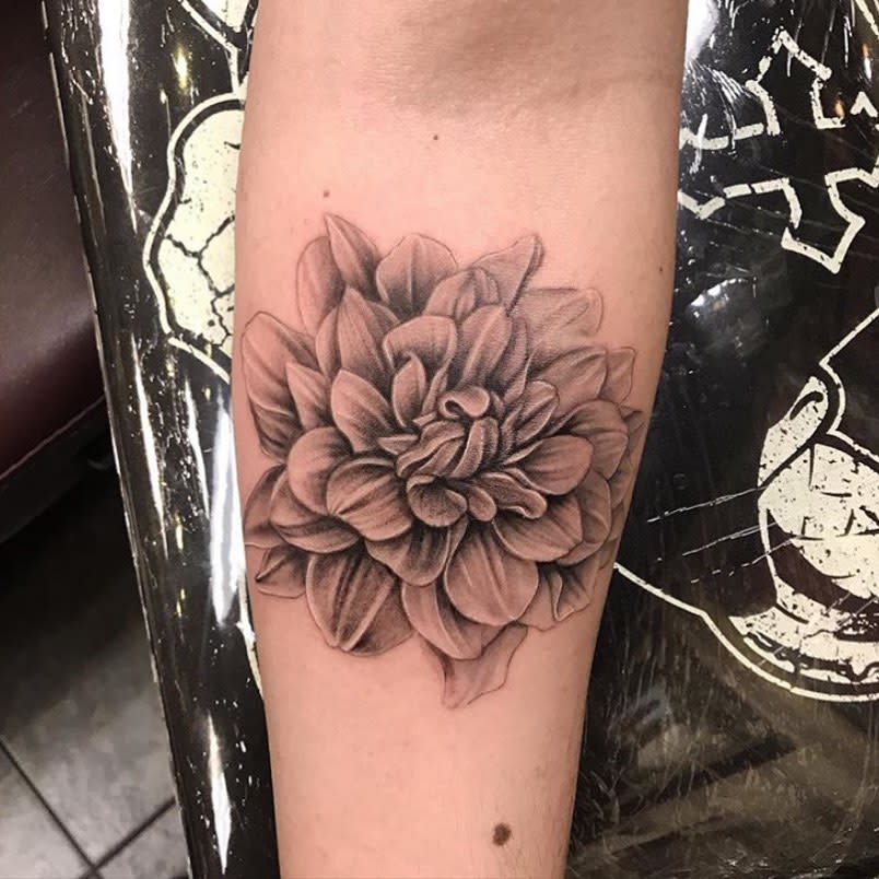 Realistic black and grey dahlia flower tattoo with intricate shading on the forearm