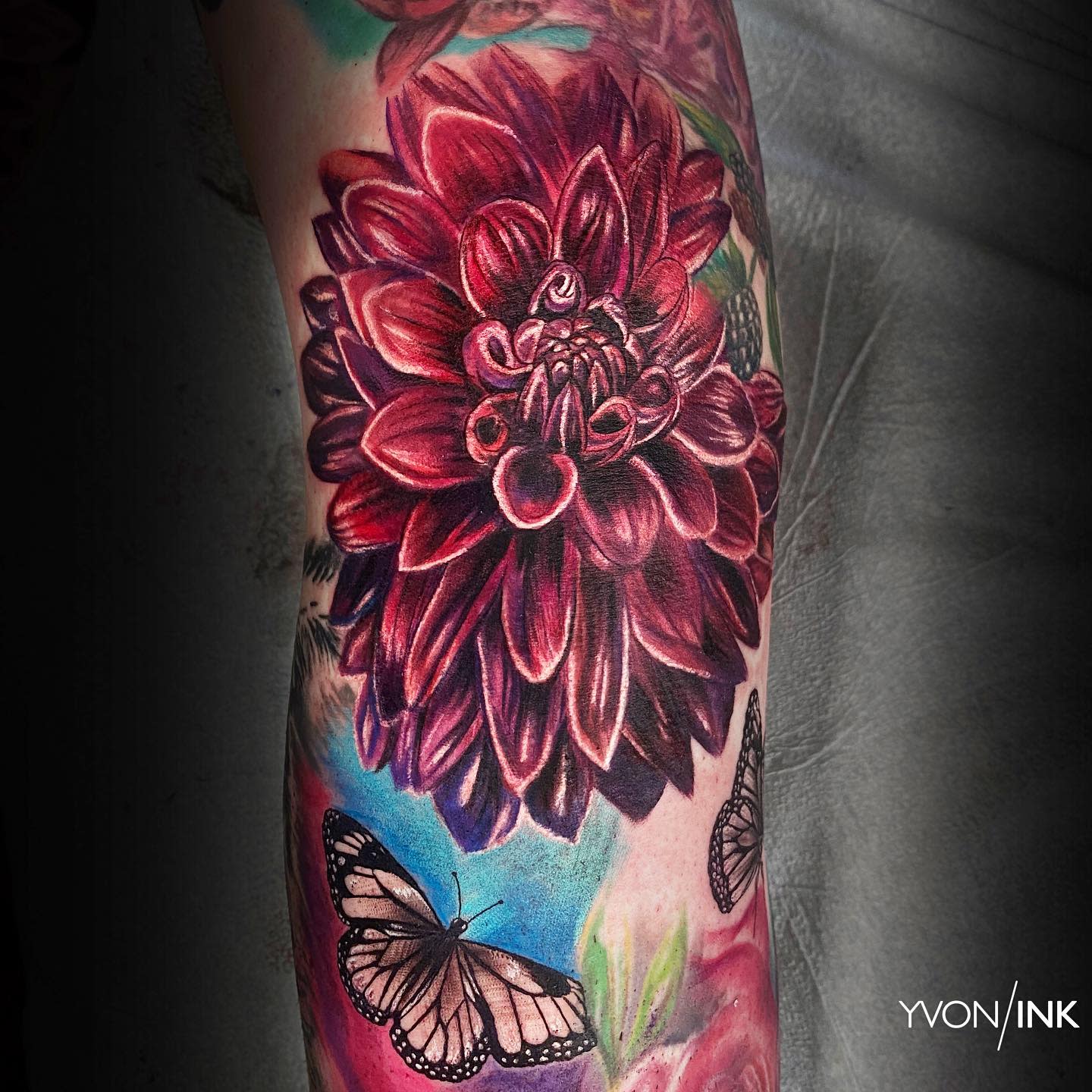 Vibrant red dahlia tattoo with rich shading, accompanied by butterflies for added contrast