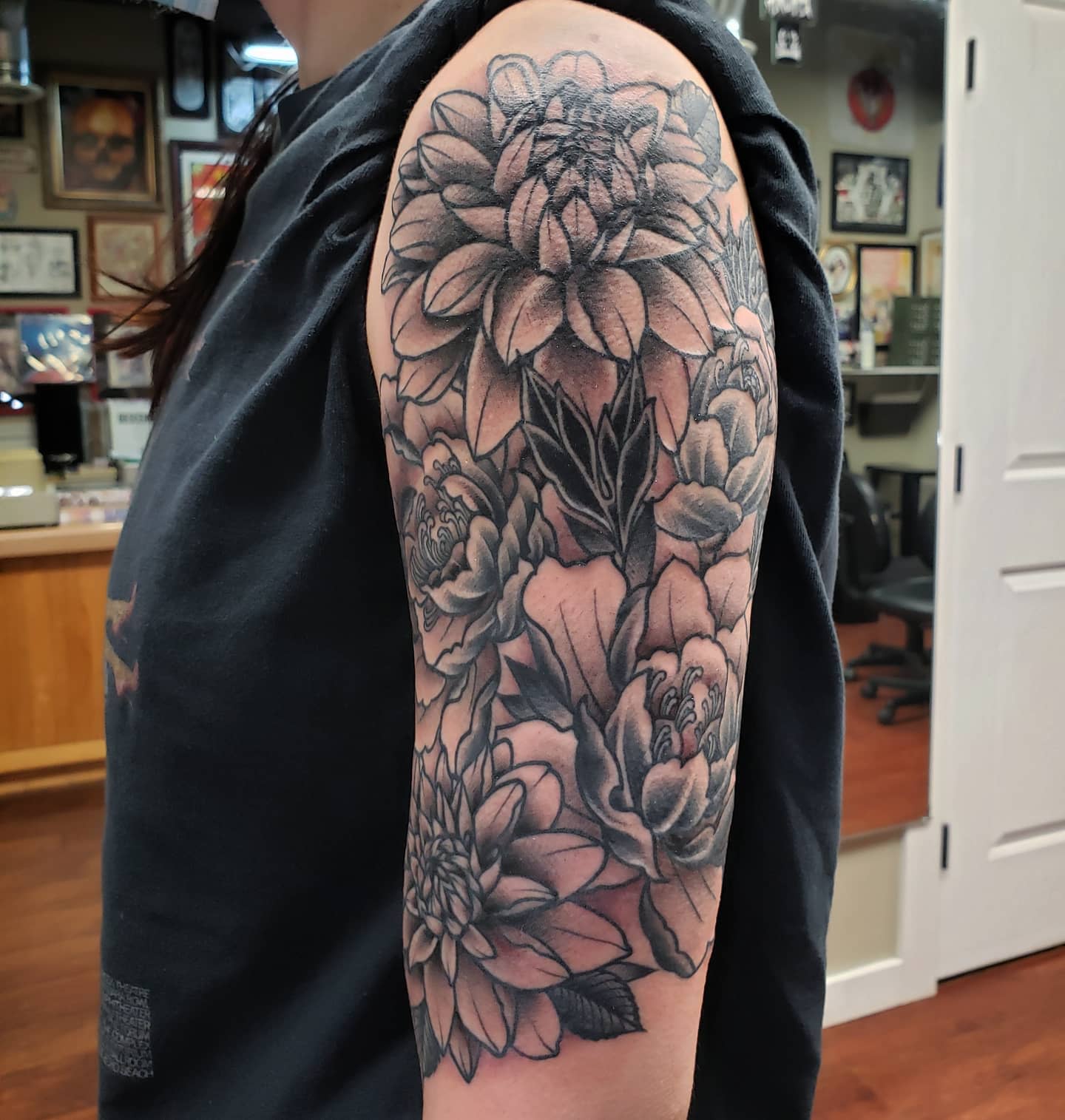 Black and grey upper arm tattoo featuring large dahlias and peonies with intricate shading