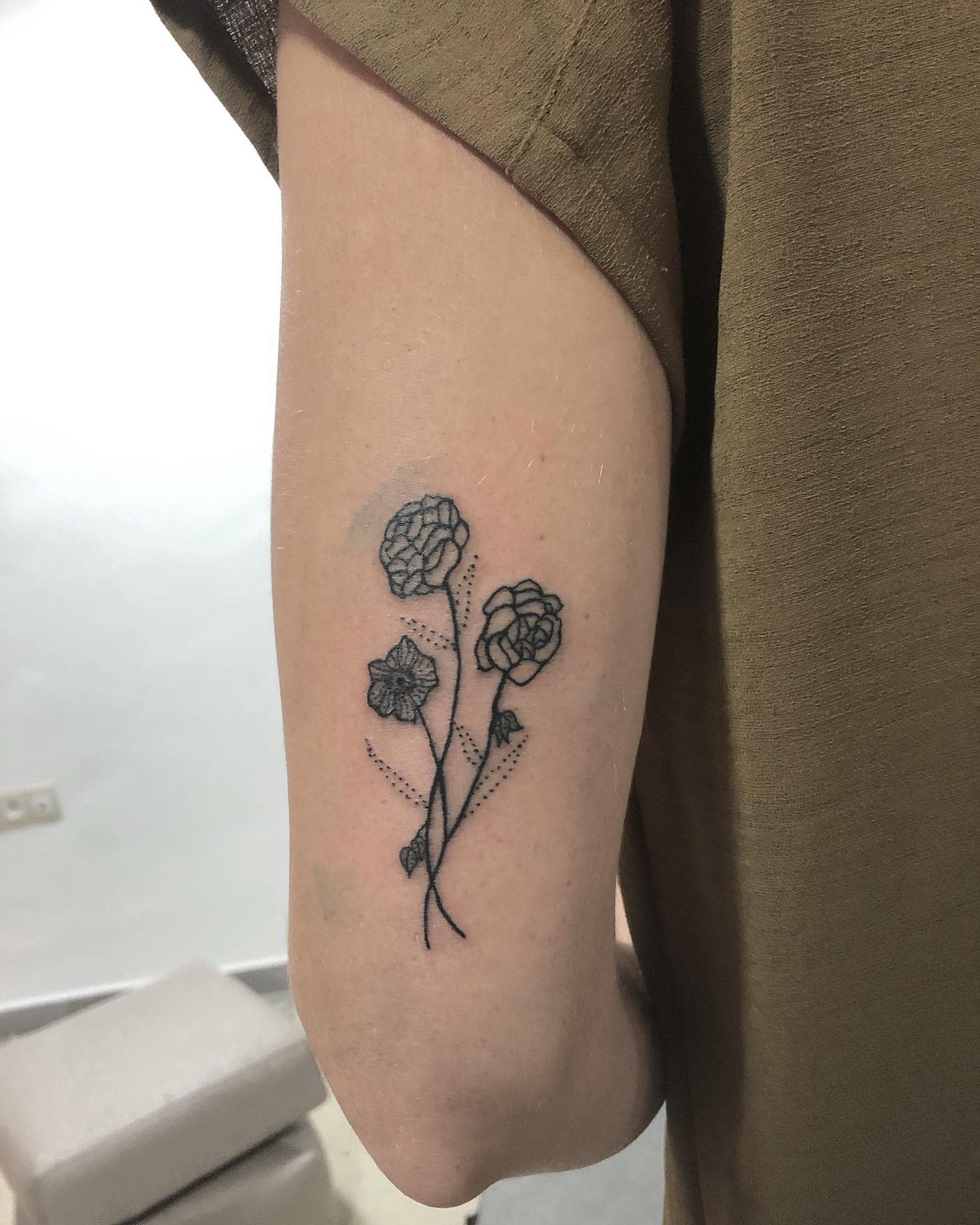Minimalist upper arm tattoo with three small flowers, including delicate dahlia designs
