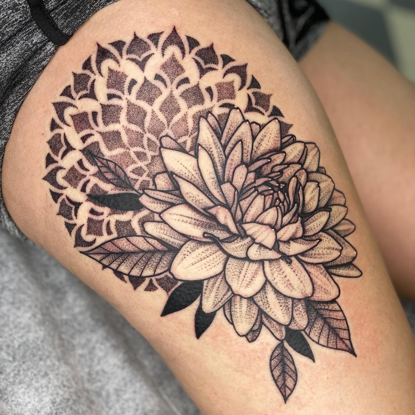 Intricate thigh tattoo featuring a detailed dahlia with a dotwork mandala background