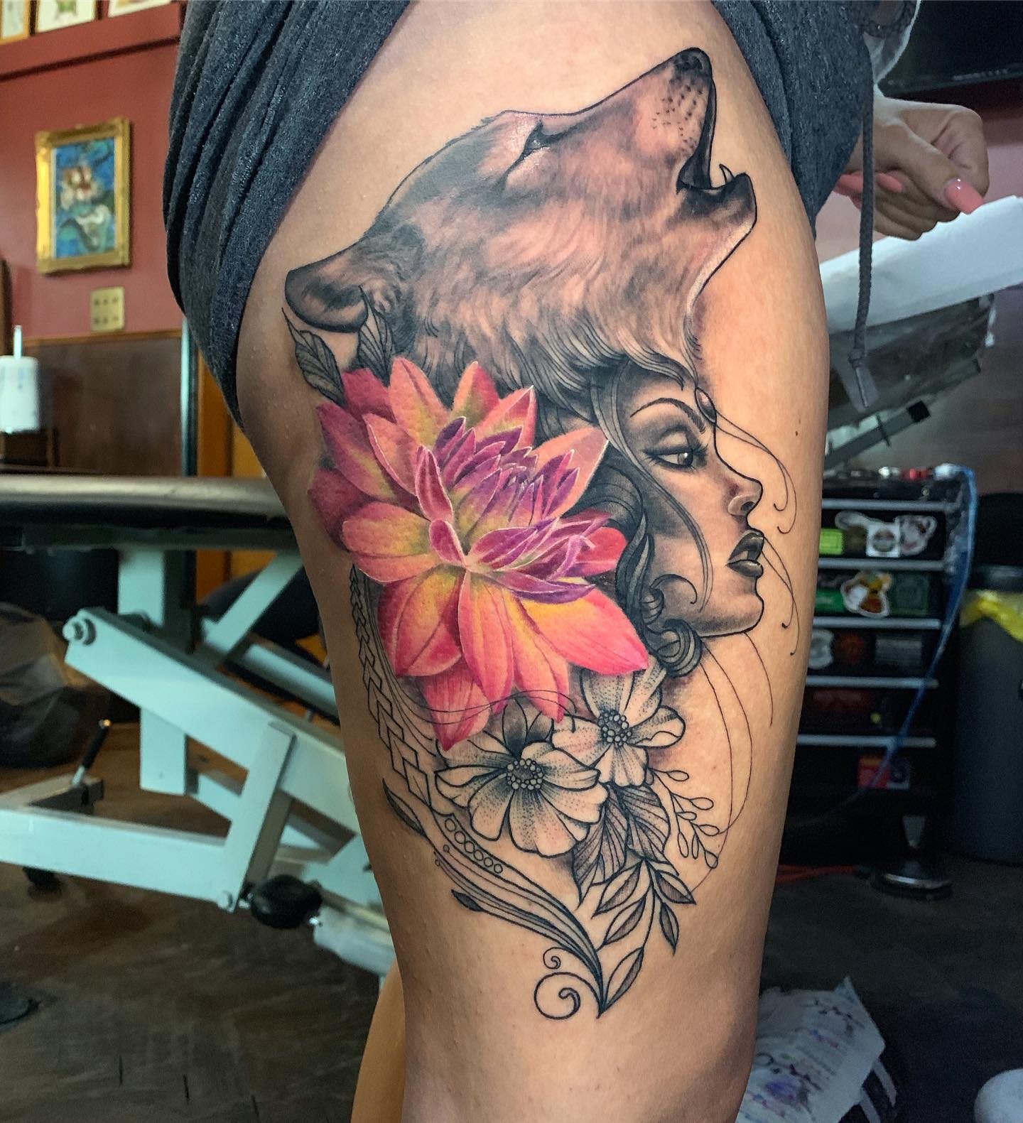 Thigh tattoo featuring a colorful dahlia, a wolf's head, and a woman's face with floral details