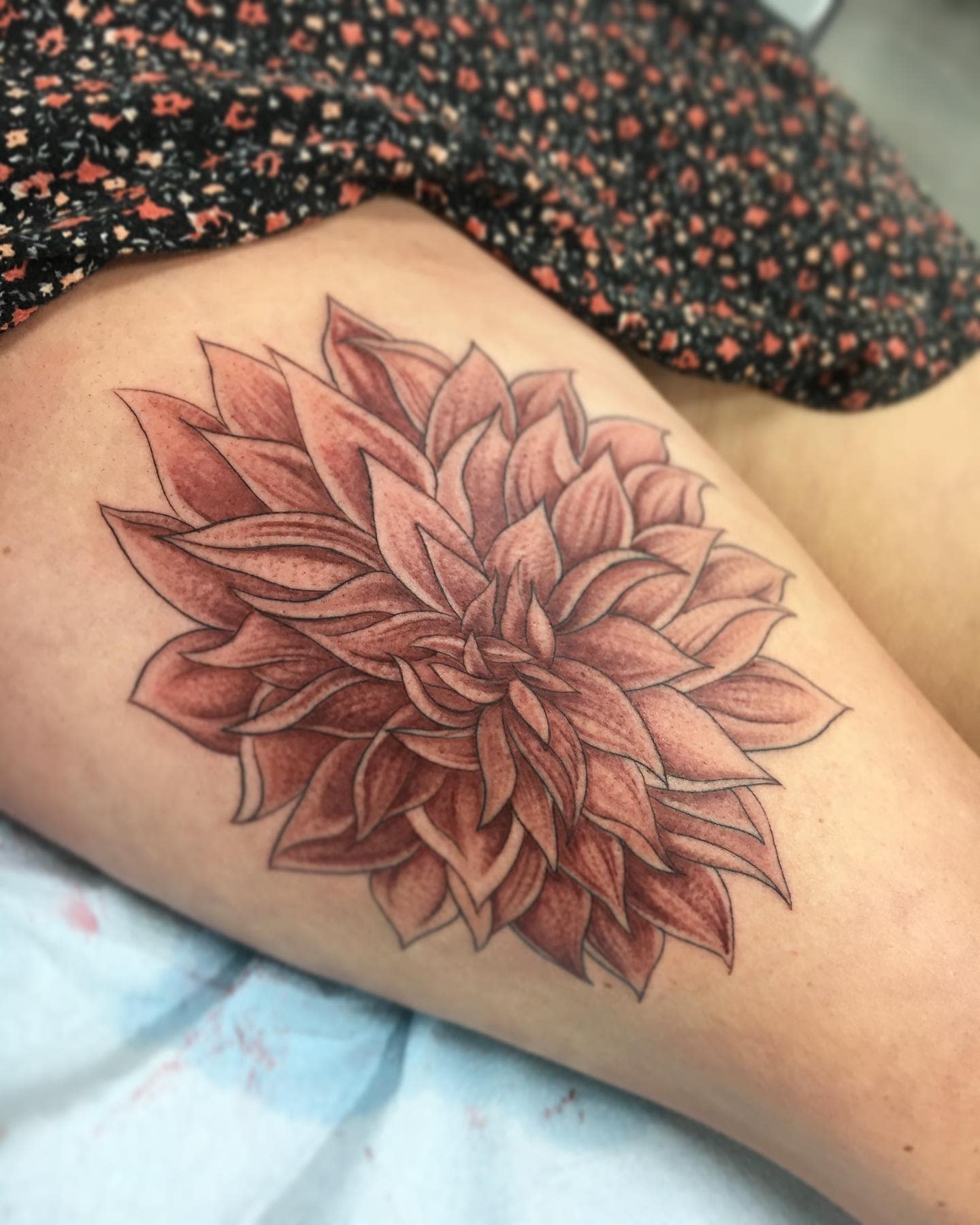 Large red dahlia tattoo on the thigh with detailed shading and dotwork for added depth