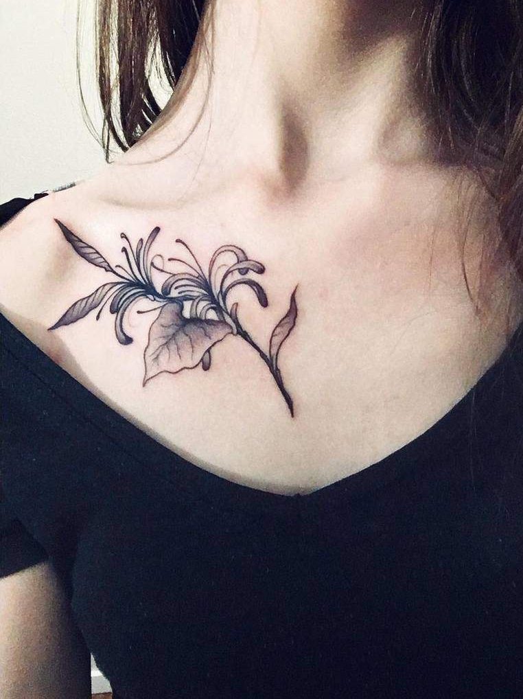 Delicate black ink honeysuckle tattoo on the collarbone, with fine lines and soft shading