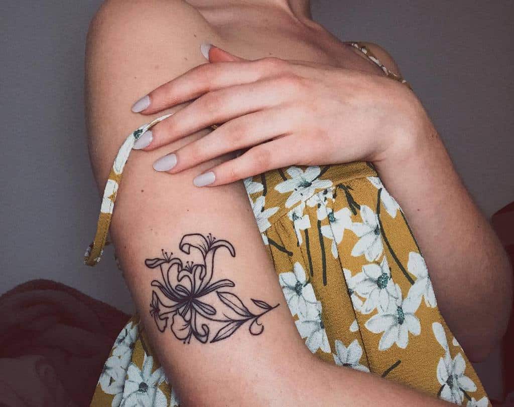 Dainty black ink honeysuckle tattoo on the upper arm with simple, flowing lines